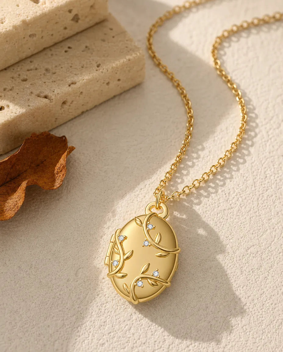 Lille oval medaljon i guldtone med blade i relief og en klar krystal siddende på hvert blad.