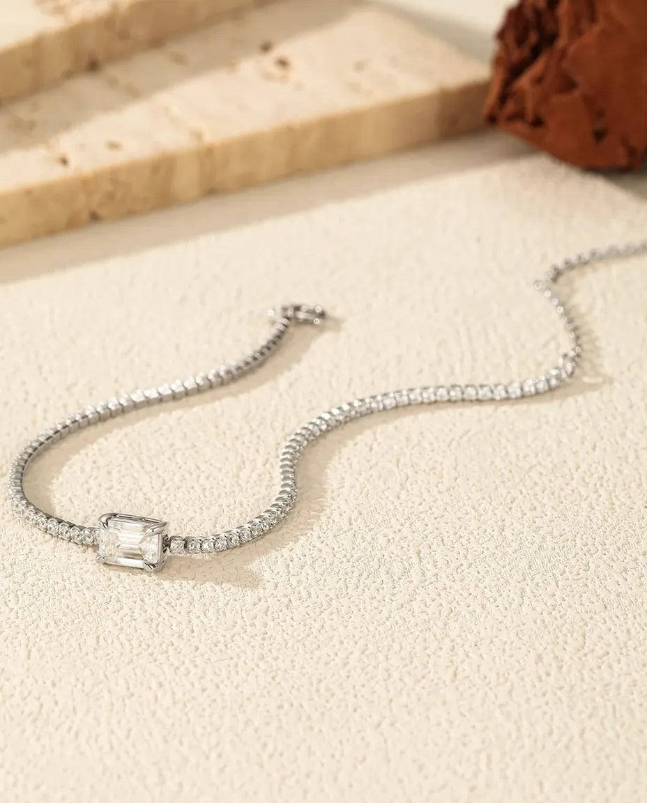 Armbånd i 925 sterling sølv med en emeraldslebet moissanite i midten og en linje af små runde sten.