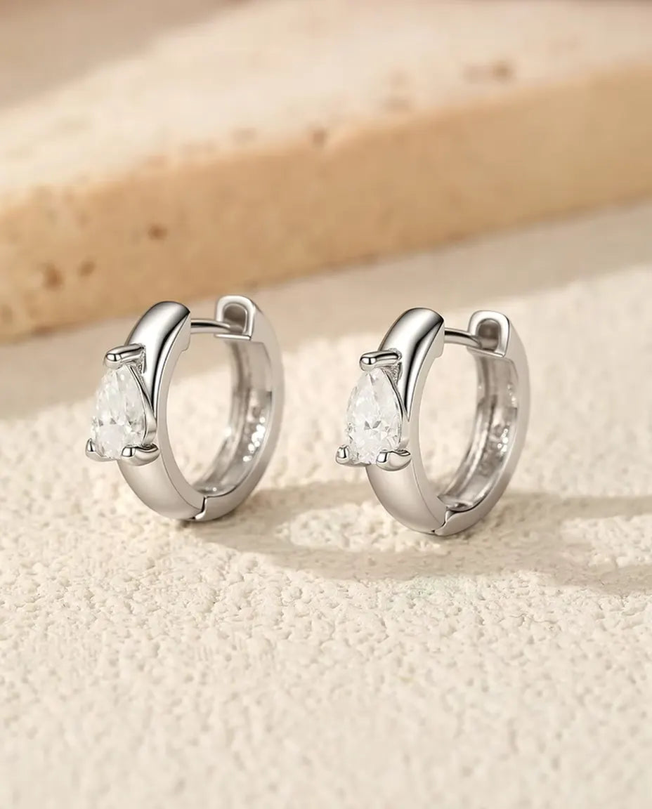 To brede huggie-creoler i 925 sterling sølv med dråbeslebet moissanite står side om side på råhvid puds foran travertin.