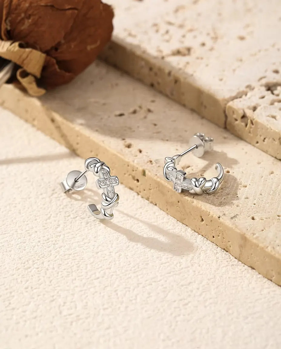 Et par C-formede øreringe i 925 sterling sølv med knuder og et lille moissanite-kors ved lys travertin og tørret rose.