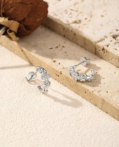Et par C-formede øreringe i 925 sterling sølv med knuder og et lille moissanite-kors ved lys travertin og tørret rose.