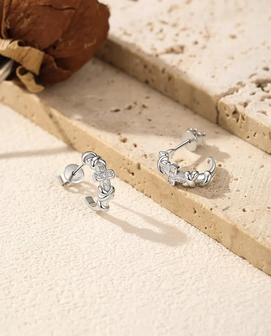 Et par C-formede øreringe i 925 sterling sølv med knuder og et lille moissanite-kors ved lys travertin og tørret rose.