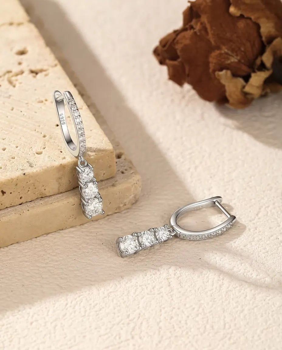 Moissanite Øreringe i 925 Sølv - den ene ørering hængende fra en travertinplade, den anden liggende ved siden af