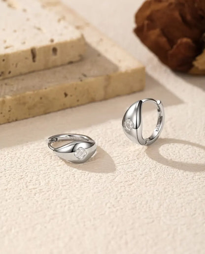 Et par små kuppelformede creoler i 925 sterling sølv med en firkantet moissanite foran, liggende og stående på råhvid puds.