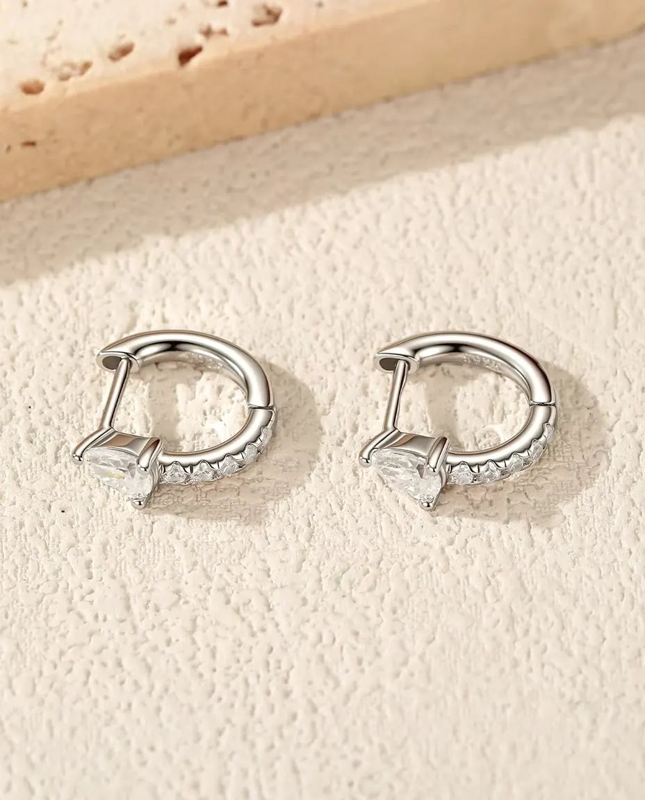 Et par små creoler i 925 sterling sølv med dråbeformet moissanite og en række zirkonia, lagt på råhvid puds ved travertin.
