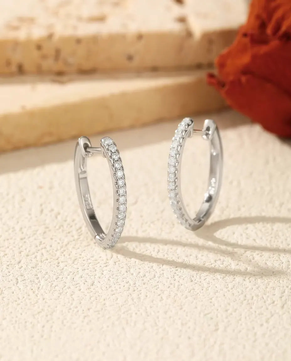 Et par U-formede creoler i 925 sterling sølv med en række små moissanite-sten, stillet op på råhvid puds ved lys travertin.