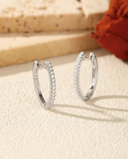 Et par U-formede creoler i 925 sterling sølv med en række små moissanite-sten, stillet op på råhvid puds ved lys travertin.