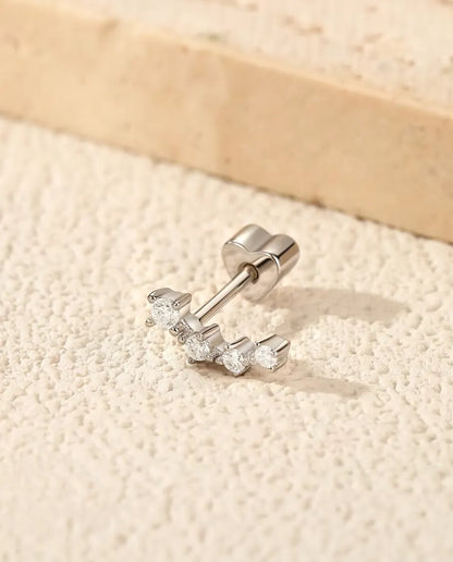 En ørestik i 925 sterling sølv med fire runde moissanite-sten i en bue, lagt på råhvid puds ved en plade af travertin.