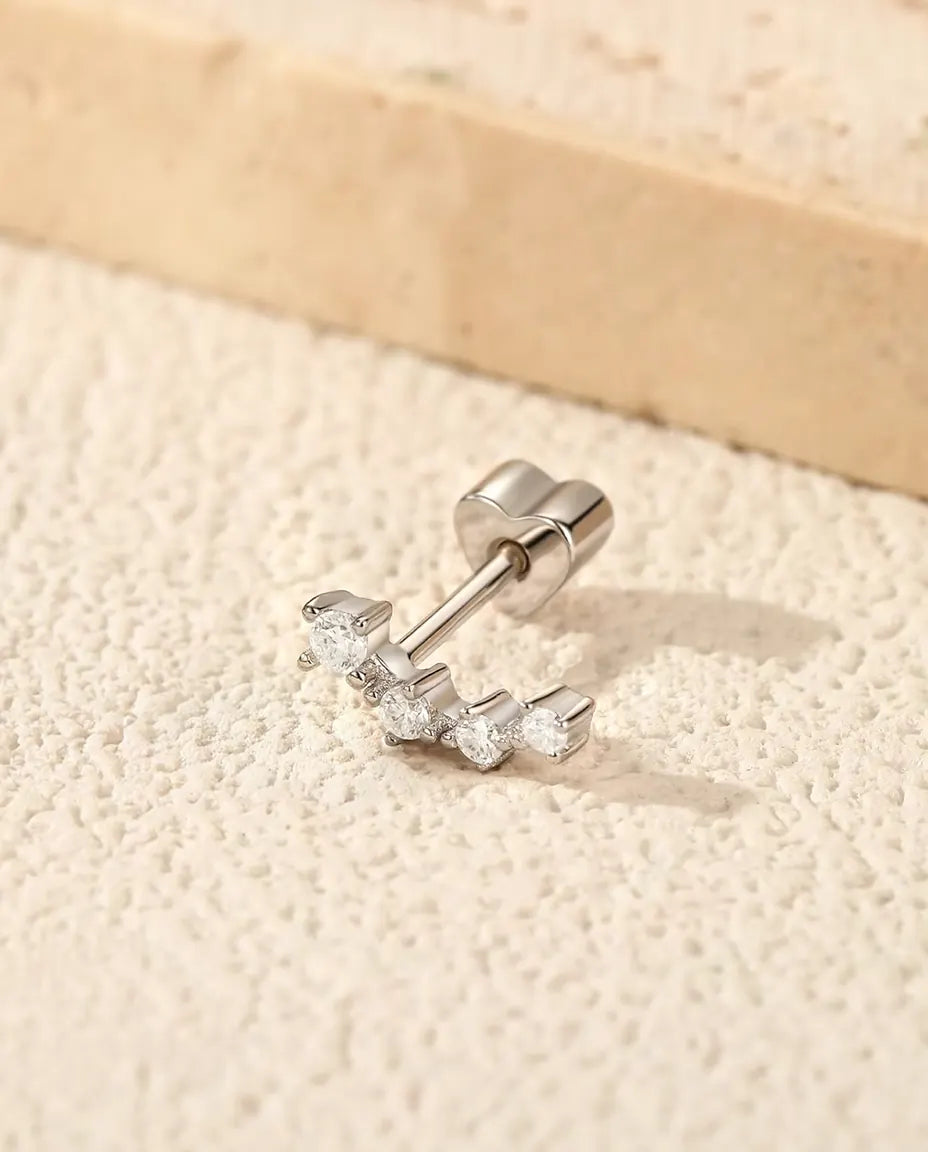 En ørestik i 925 sterling sølv med fire runde moissanite-sten i en bue, lagt på råhvid puds ved en plade af travertin.