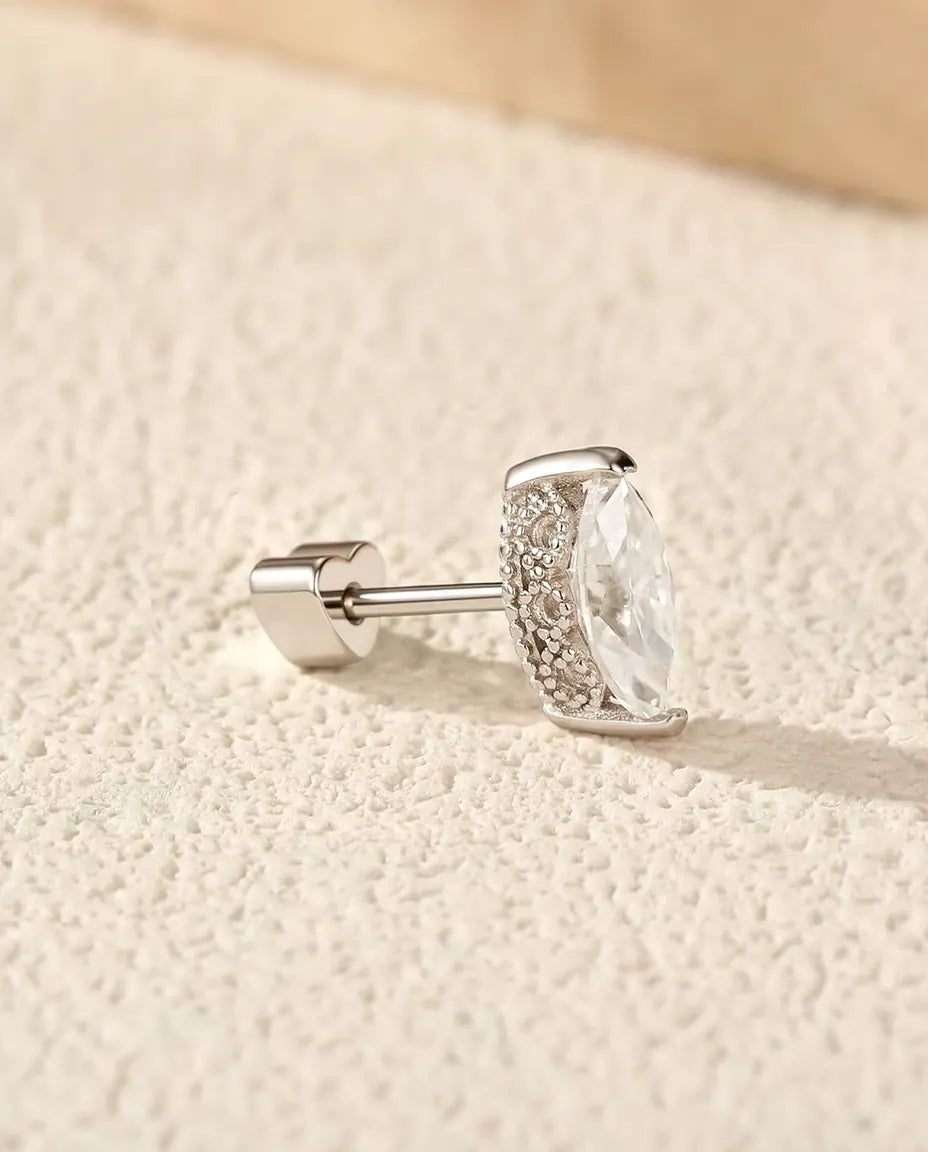 En ørestik i 925 sterling sølv med en marquisesleben moissanite og kornet sølvside, lagt på råhvid puds ved travertin.