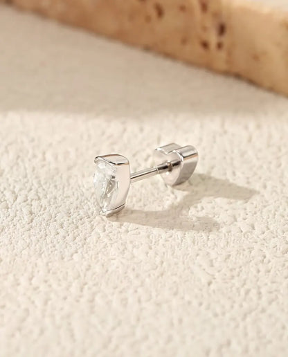 En dråbeformet ørestik med moissanite i 925 sterling sølv ligger på siden på råhvid puds, med den hjerteformede lås bagud.