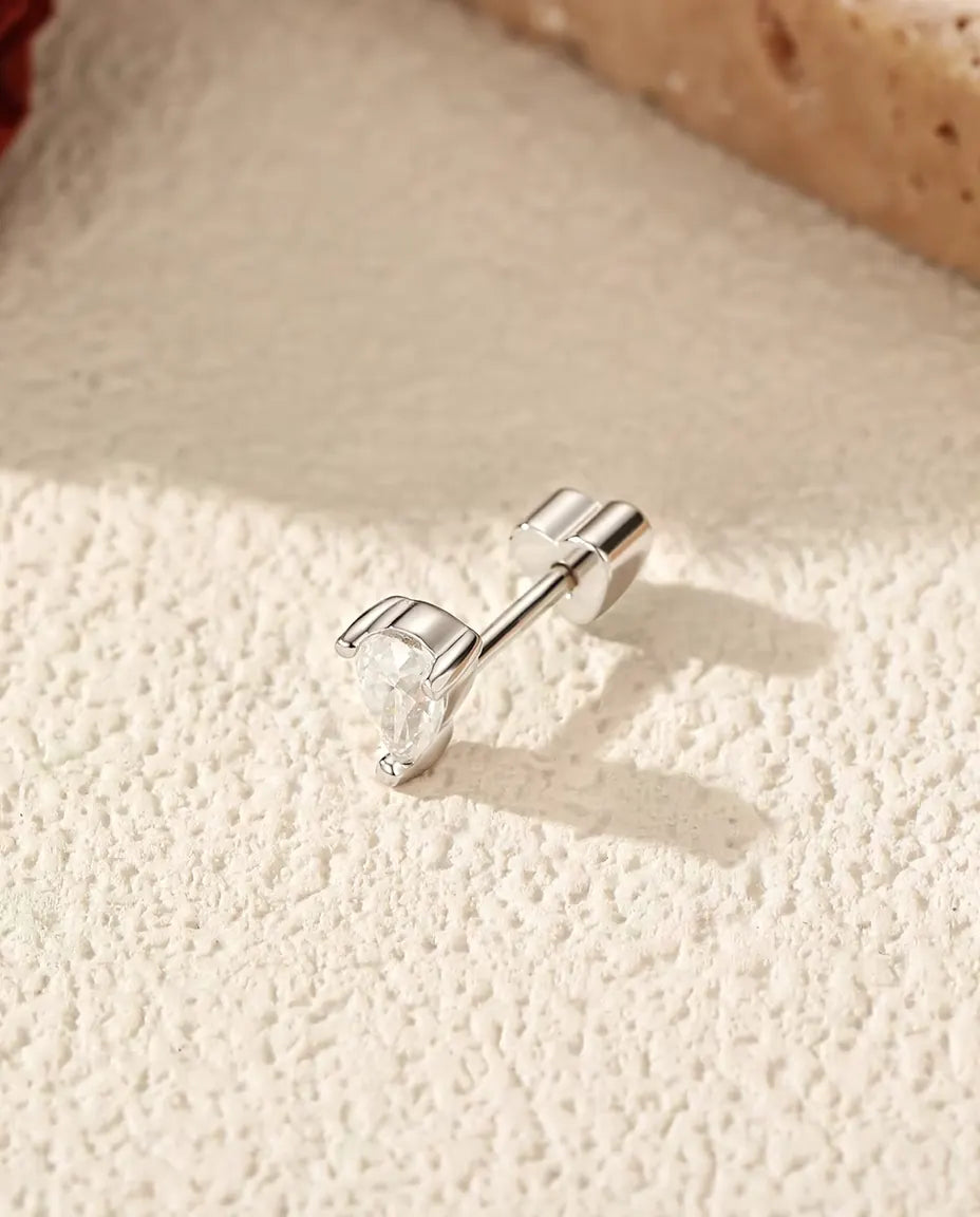 En dråbeformet moissanite ørestik i 925 sterling sølv med hjerteformet lås på råhvid puds ved en tørret rose og travertin.