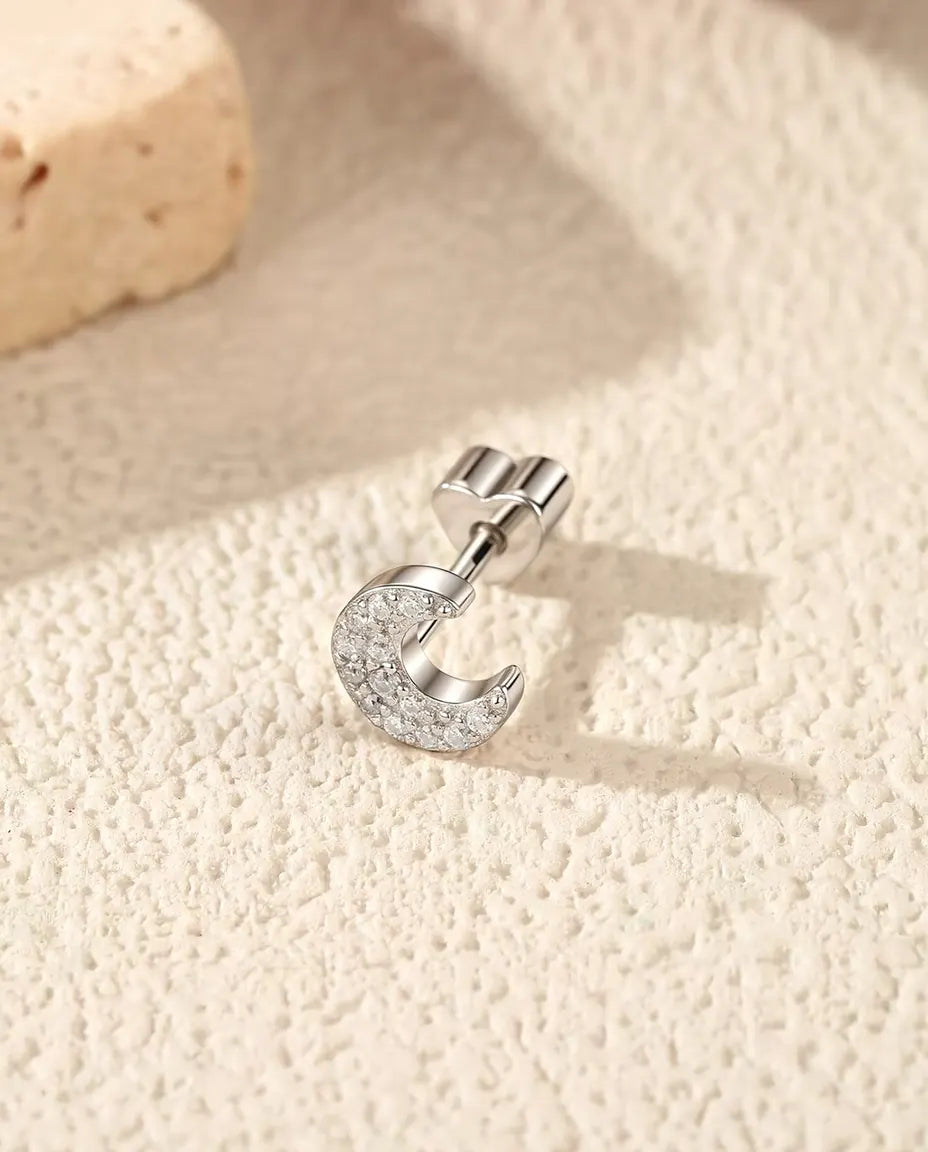 En halvmåneformet ørestik med pavé af moissanite i 925 sterling sølv ligger på siden på råhvid puds foran lys travertin.