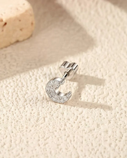 En halvmåneformet ørestik med pavé af moissanite i 925 sterling sølv ligger på siden på råhvid puds foran lys travertin.