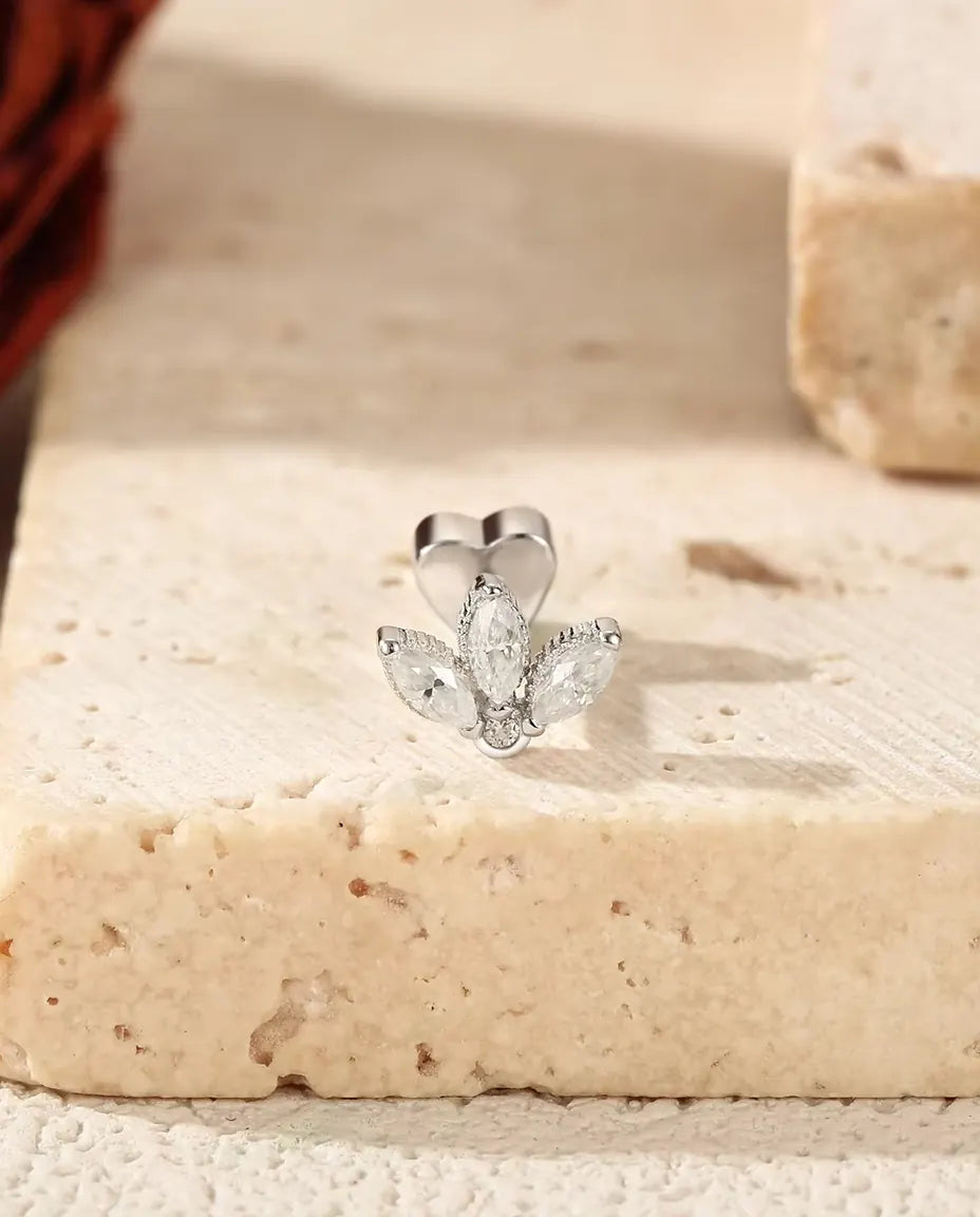 En lotusformet ørestik med tre marquise-slebne moissanite-sten i 925 sterling sølv står på lys travertin ved en tørret rose.
