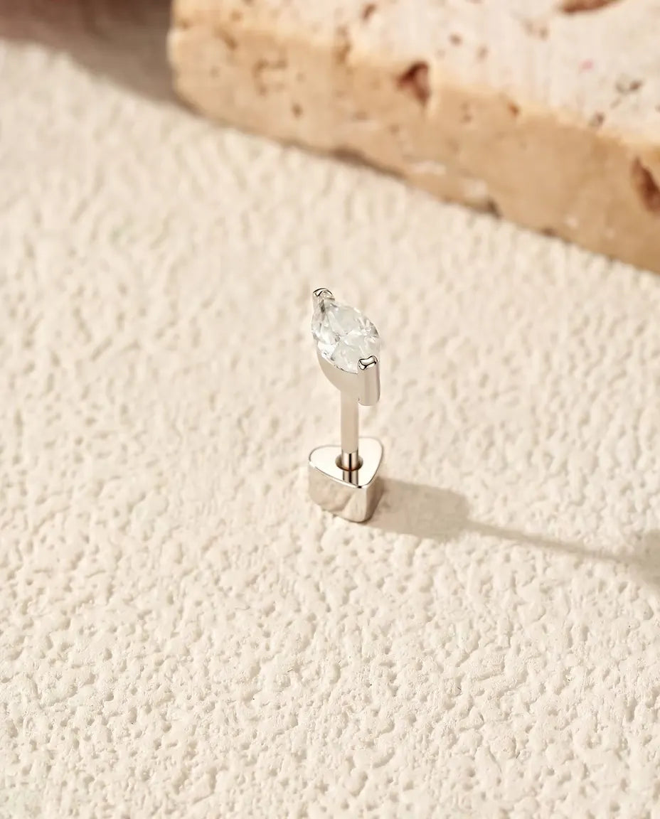 En marquiseformet moissanite ørestik i 925 sterling sølv med hjerteformet lås står på råhvid puds foran lys travertin.