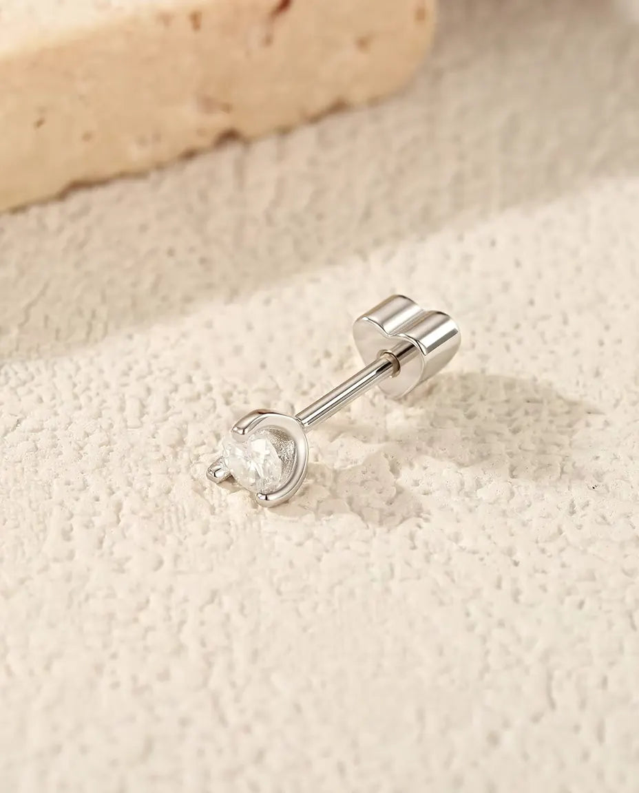 En rund moissanite-ørestik med sølvbue i 925 sterling sølv ligger på siden med sin hjerteformede lås på råhvid puds.