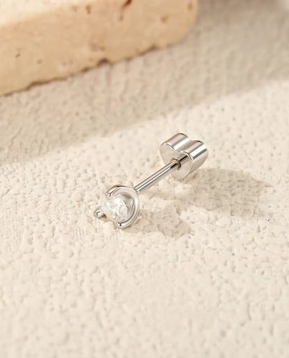 En rund moissanite-ørestik med sølvbue i 925 sterling sølv ligger på siden med sin hjerteformede lås på råhvid puds.