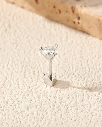 En rund moissanite-ørestik med tre kløer i 925 sterling sølv står på sin hjerteformede lås på råhvid puds foran travertin.