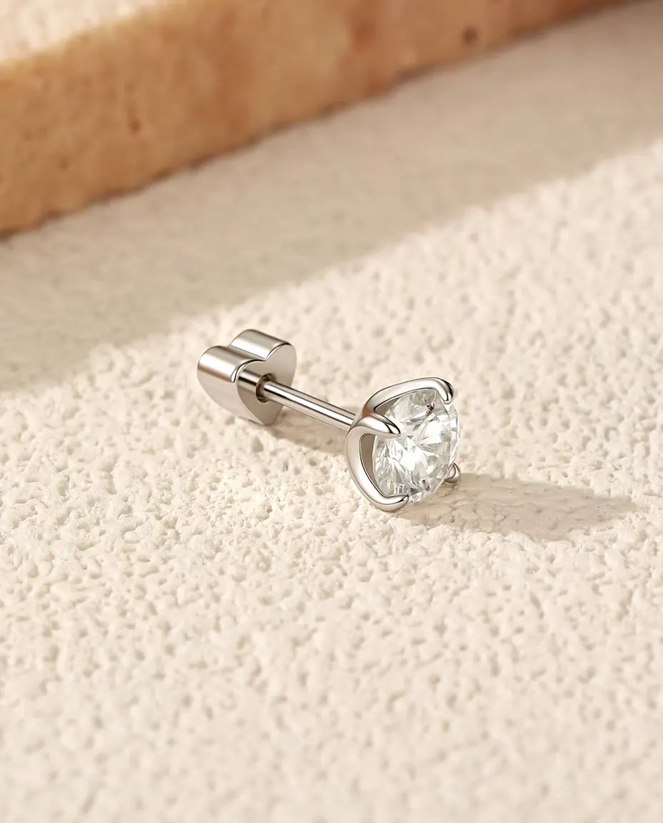 En rund moissanite-ørestik med fire kløer i 925 sterling sølv ligger med hjerteformet lås på råhvid puds ved travertin.
