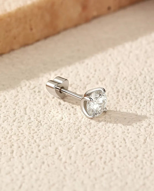 En rund moissanite-ørestik med fire kløer i 925 sterling sølv ligger med hjerteformet lås på råhvid puds ved travertin.