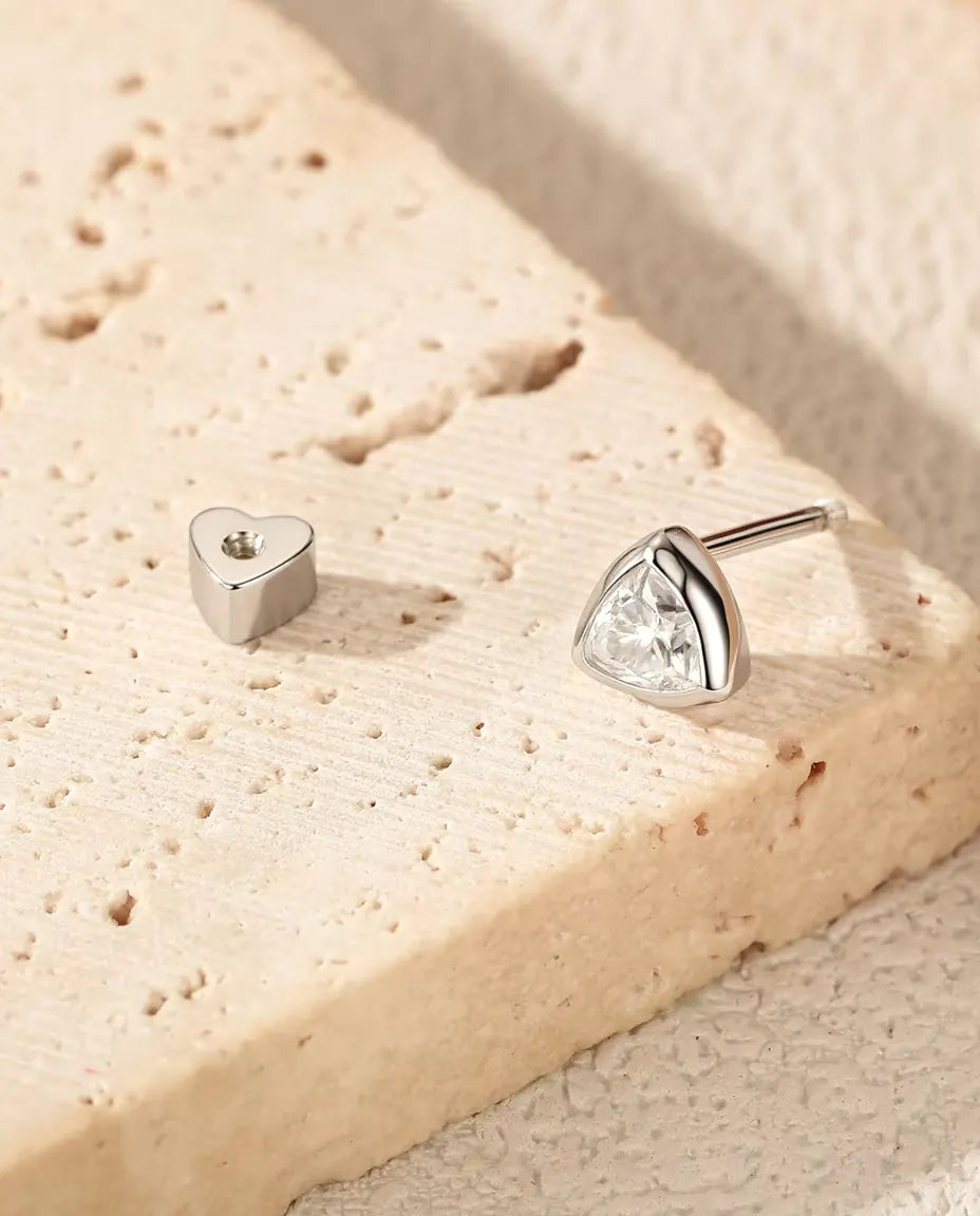 En trekantet moissanite-ørestik i 925 sterling sølv ligger på lys travertin, adskilt fra sin hjerteformede lås.