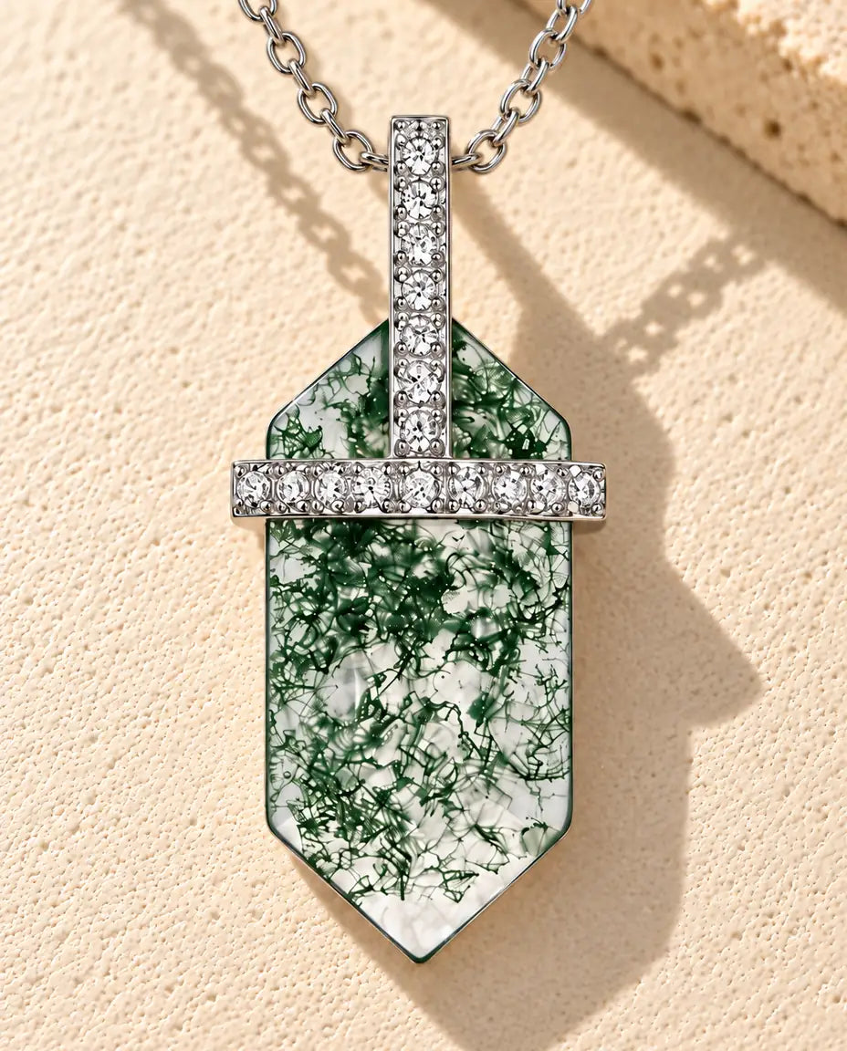 Sølvhalskæde med en klar sekskantet moss agate, en sølvbarre med små hvide zirkonia og T-øsken på beige puds foran travertin.
