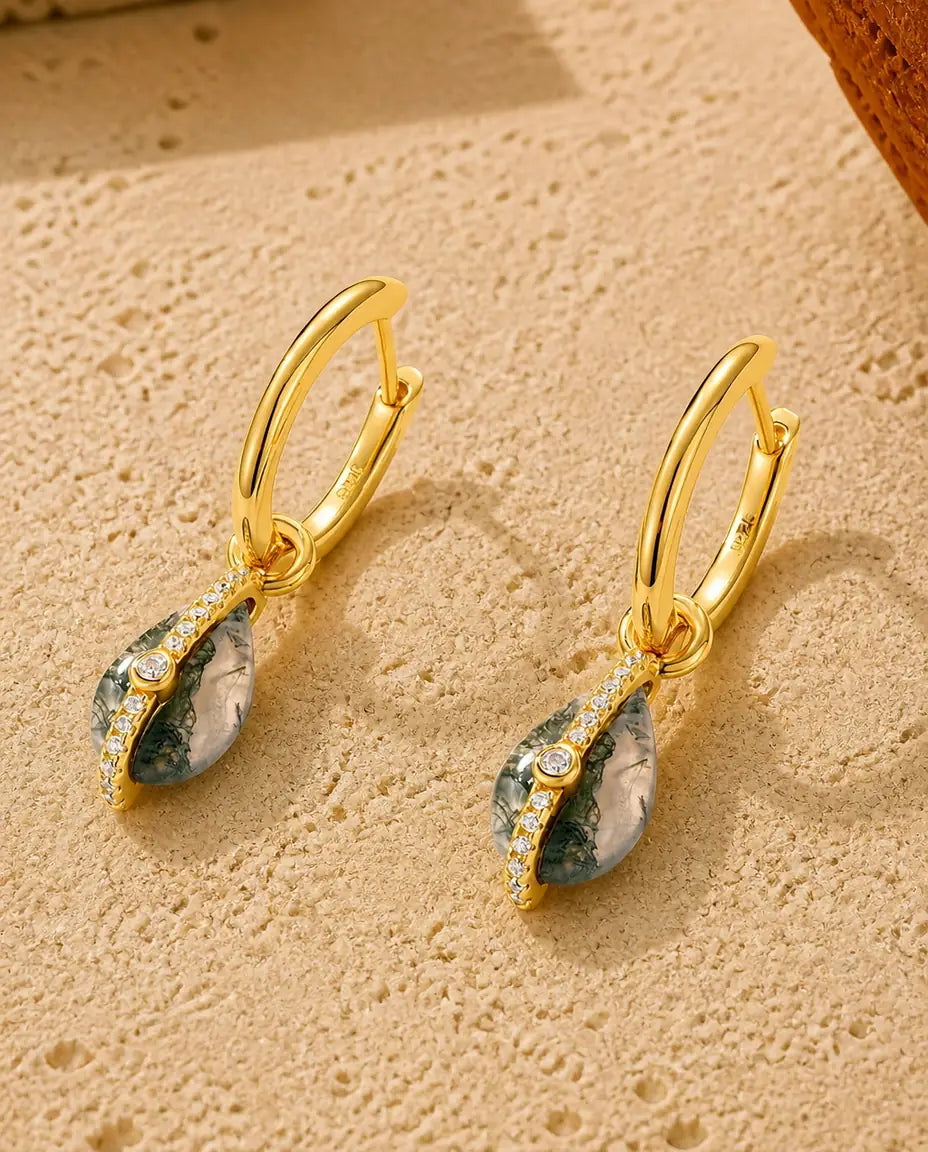 Guldbelagte creoler med en dråbeformet grøn moss agate-cabochon og en række små klare sten langs kanten.