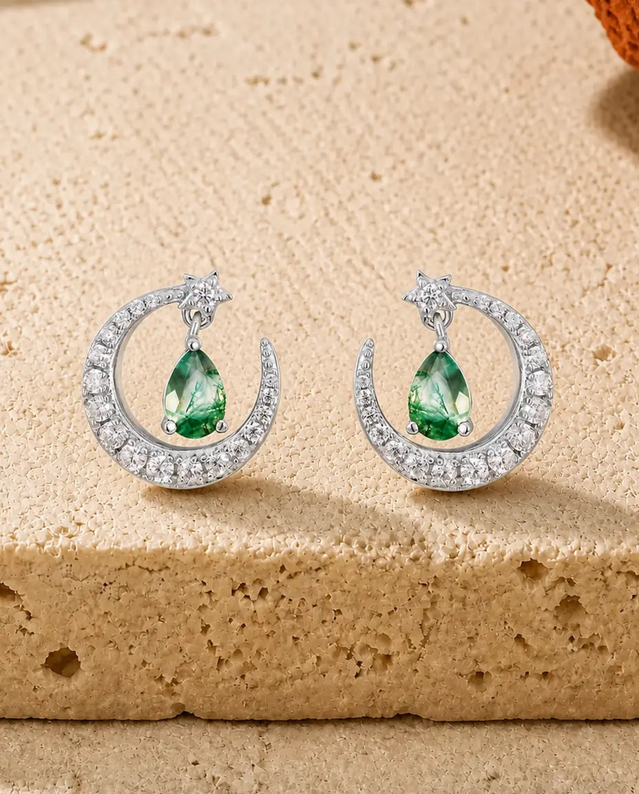 Sølvøreringe med pavésat månesegl, lille stjerne og en grøn moss agate-dråbe, der svinger frit i buen.