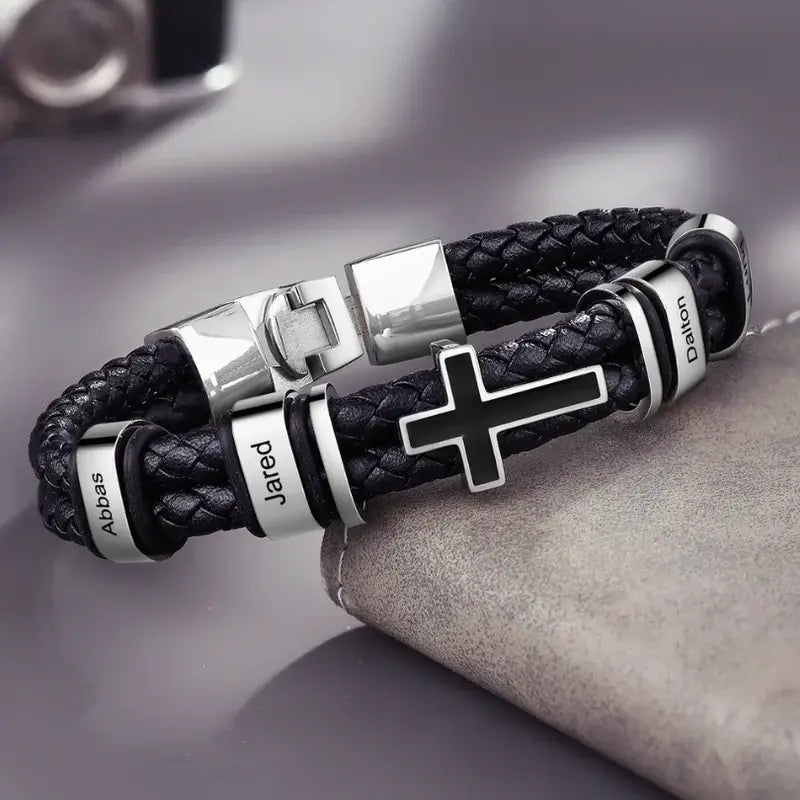 Sort læderarmbånd til mænd med børstede stålled, en lille korscharm og indgraverede navne.