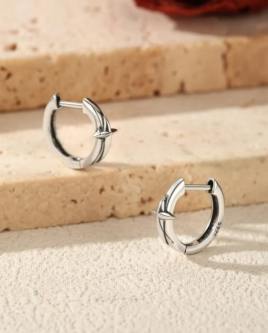 To små creoler i 925 sterling sølv med en firtakket stjerne ligger på et lyst trin af travertin, med en tørret rose bagved.
