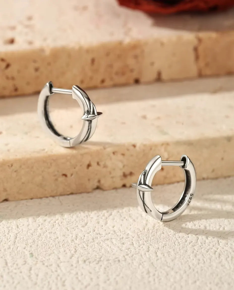 To små creoler i 925 sterling sølv med en firtakket stjerne ligger på et lyst trin af travertin, med en tørret rose bagved.