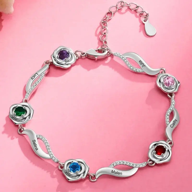 Sølvfarvet armbånd i kobber med en blomstercharm, et indgraveret navn og farvede fødselssten.