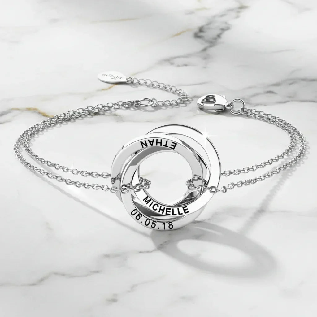 Armbånd med tre sammenflettede ringe i 925 sterling sølv, hvor hver ring bærer en indgraveret tekst.