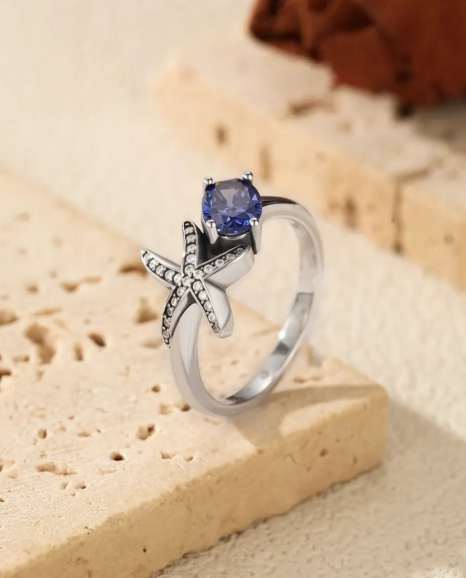 Sølvring med femarmet søstjerne i klare zirkoner ved siden af en oval lilla sten i 925 sterling sølv.